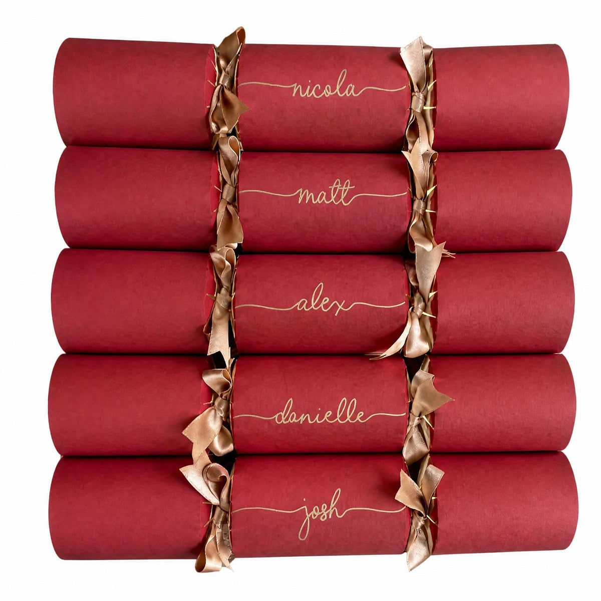 A collection of eight personalised red paper party Christmas crackers tied with double satin gold ribbon, each handwritten with a different name in gold ink, on a solid white background.